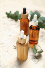 Bottles with cosmetic oil and eucalyptus branches on textured background