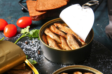 Board of canned smoked sprats on dark background