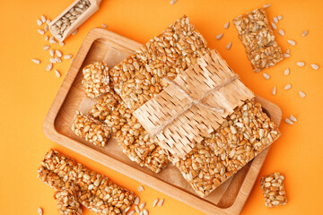 Board with tasty kozinaki and sunflower seeds on orange background