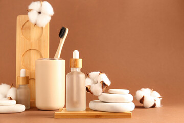 Bottles of essential oil, toothbrush, spa stones and cotton flowers on color background