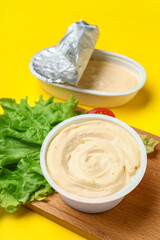 Wooden board with box of processed cheese and vegetables on yellow background
