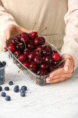 Woman holding plastic container with ripe cherries at table