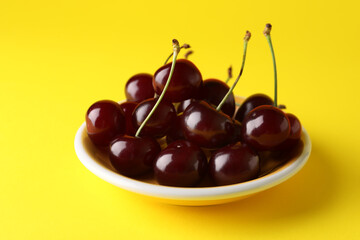 Plate with sweet cherries on yellow background