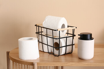 Basket with toilet paper rolls and bottle of soap on wooden table near color wall, closeup
