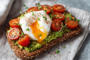 Creamy avocado toast whole grain bread topped with poached egg and cherry tomatoes