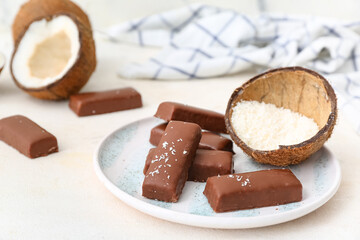 Plate with tasty chocolate covered coconut candies on white background