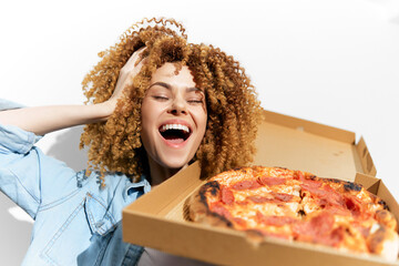 Happy young woman with curly hair enjoying pizza, wearing a denim jacket, against a light background, cheerful atmosphere, food concept, seasonal comfort food