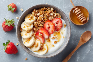 Creamy yogurt bowl with granola, fresh strawberries, and banana slices, drizzled with honey