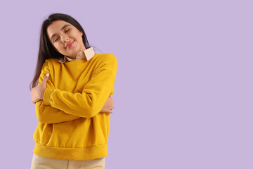 Beautiful young happy woman hugging herself on lilac background