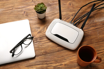 Modern wi-fi router with laptop and cup of tea on wooden background