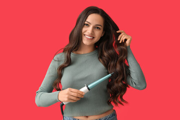 Beautiful young woman with curling iron on red background