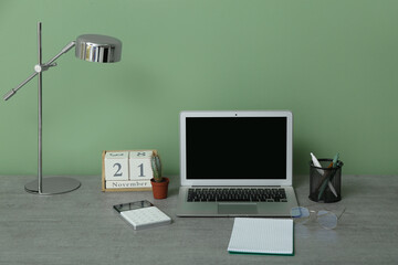 Modern office workplace with laptop, calendar and lamp near green wall