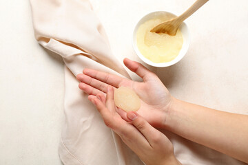 Woman applying scrub onto her hands on light background, closeup