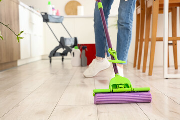 Young woman with cleaning supplies in trolley mopping floor at home, closeup
