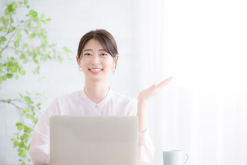 パソコンの前でカメラ目線の笑顔の女性　オフィスカジュアルのイメージ　ピンクのシアーシャツのかわいい女性	　オススメのポーズ