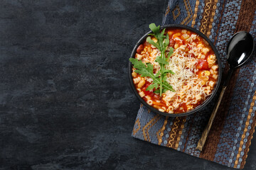Bowl of pasta fagioli with cheese and arugula on black background