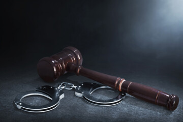 Handcuffs and judge gavel on dark smoke background