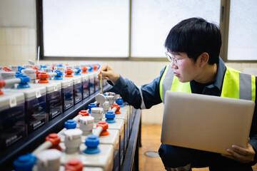 Technician performs maintenance on backup power system battery while holding laptop in industrial...