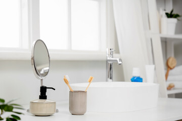Holder of toothbrushes with soap and mirror near sink on table in bathroom