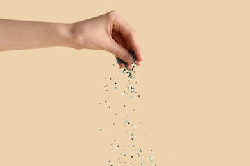Female hand with beautiful blue confetti on beige background