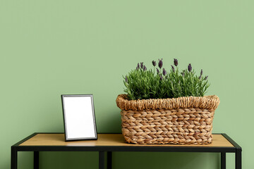 Pot with lavender and photo frame on shelving unit against green background
