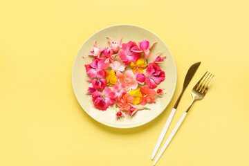 Plate with different beautiful edible flowers and cutlery on yellow background