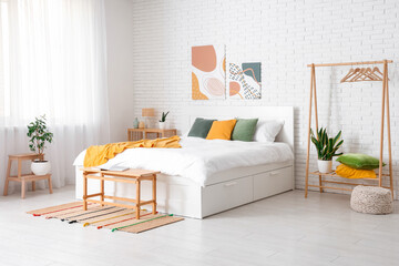 Interior of light room with big bed, paintings and clothes rack
