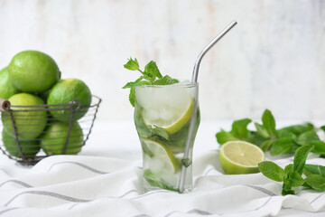 Glass of fresh Mojito cocktail with mint and basket of limes on white background