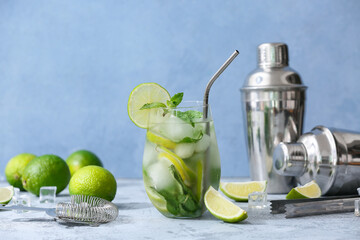 Glass of fresh Mojito cocktail with limes and mint on blue background
