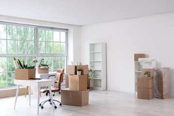 Interior of light office with workplace, shelf units and cardboard boxes on moving day