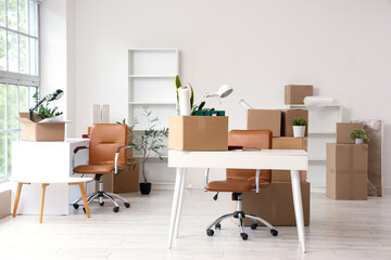 Interior of light office with workplace, shelf units and cardboard boxes on moving day