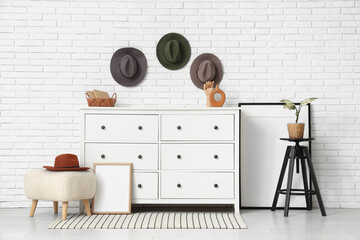 Interior of living room with stylish hats, commode and pouf