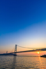 Obraz premium 春の舞子公園から見た明石海峡大橋と夕日 兵庫県神戸市 Akashi Kaikyo Bridge and sunset seen from Maiko Park in spring. Hyogo Pref, Kobe City.