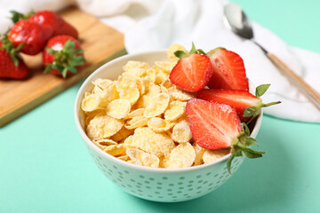 Bowl of tasty cornflakes and strawberry on turquoise background, closeup