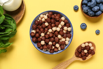Bowl of tasty chocolate corn balls, spoon and berries on yellow background, closeup