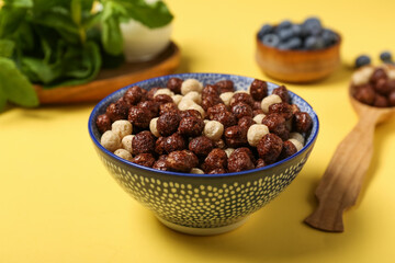 Bowl of tasty chocolate corn balls on yellow background, closeup