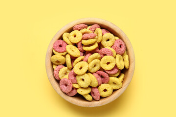 Wooden bowl with color cereal rings on yellow background, closeup