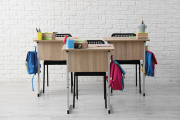 School desks with books and backpacks near white brick wall