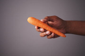 Hand holding a fresh carrot in a neutral background