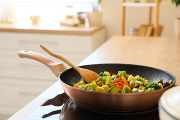 Frying pan with tasty vegetables on stove in kitchen, closeup