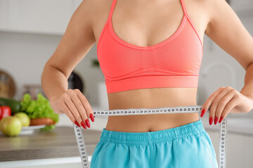 Sporty young woman with tape measure in kitchen, closeup. Diet concept