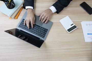 A man in a suit is sitting at a desk with a laptop and a calculator. He is holding a piece of paper and he is working on some financial documents. Concept of professionalism and focus
