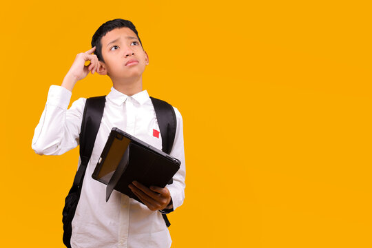 Confused Asian Student Boy Wear Backpack Holding Digital Tablet And Thinking While Looking Up