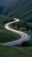 A winding road through green hills with light trails from passing cars at dusk or early evening