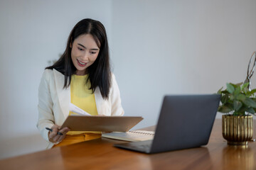A woman is sitting at a desk with a laptop and a notebook