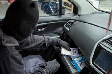 Side View Of Criminal Man In Balaclava And Gloves Stealing Cash From The Dashboard Of A Vehicle
