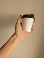 Copo de papel de café, com tampa preta, segurado por uma mão magra e de pele branca