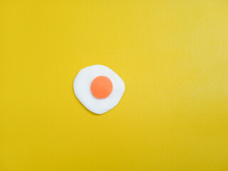 Handmade fried egg clay isolated on yellow background. Artificial food craft