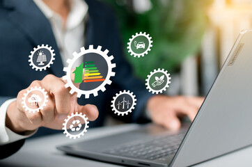 Energy efficiency icons on laptop screen, green smart home hologram in front. Represents...