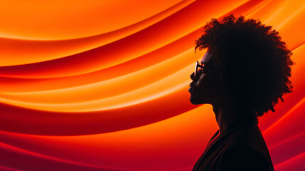 Profile view of a silhouette of an individual with curly hair and glasses, complemented by a vivid abstract orange backdrop, evoking modernity and thoughtful emotion.
